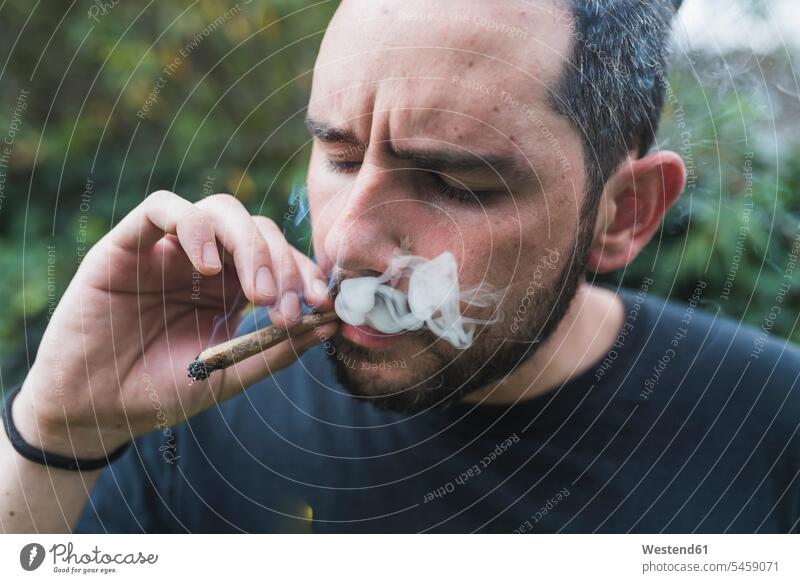 Handsome man smoking marijuana joint outdoors color image colour image location shots outdoor shot outdoor shots day daylight shot daylight shots day shots