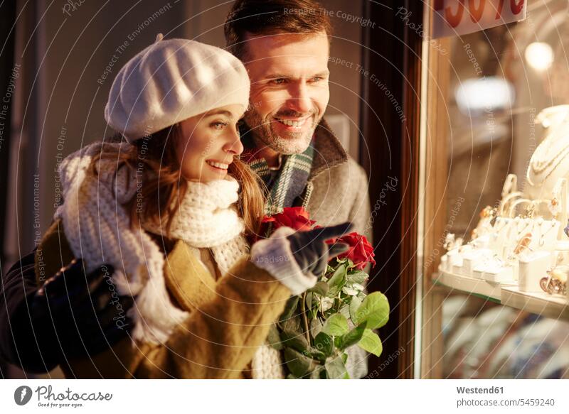 Smiling couple looking in shop window of jewellery store at Christmas time twosomes partnership couples christmas time yule-tide yuletide window display