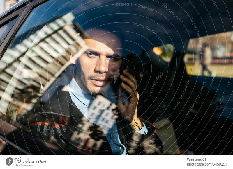 Man sitting on back seat of a car talking on cell phone on the phone call telephoning On The Telephone calling automobile Auto cars motorcars Automobiles