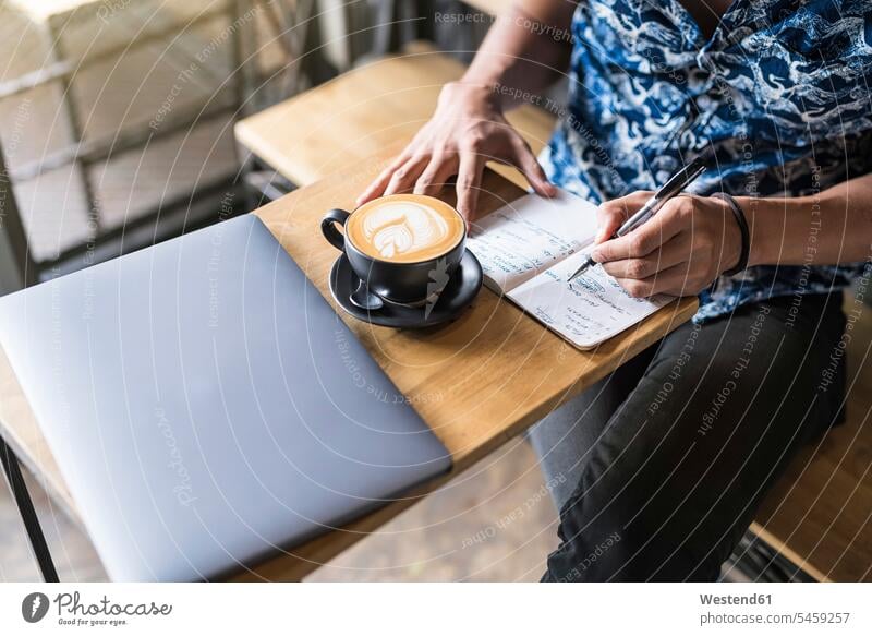 Artist writing into notebook in a cafe with coffee and laptop on the table Laptop Computers laptops sketchbook Sketch Pad sketch-pad sketch-book sketch-books