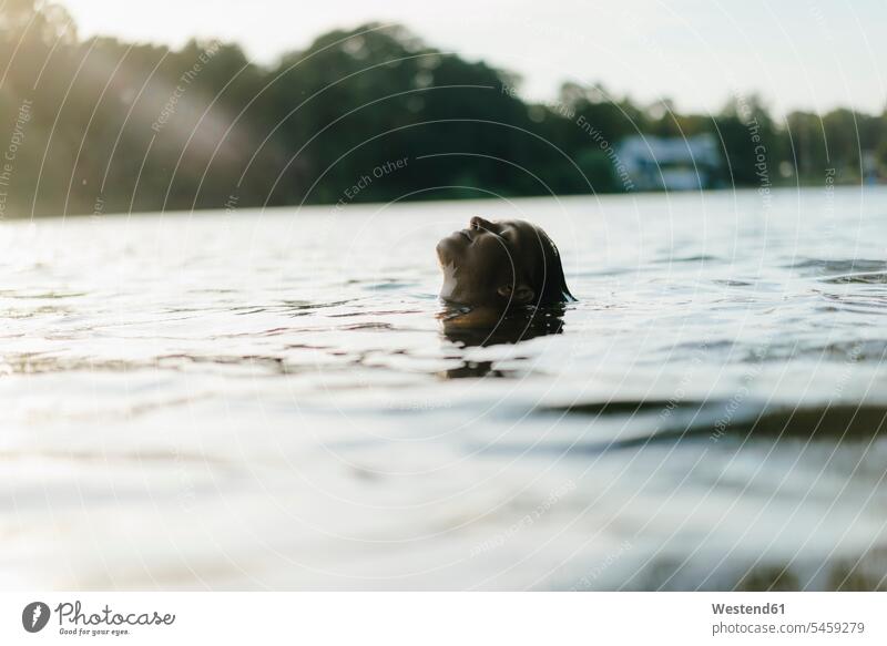 Woman floating in a lake at sunset lakes drifting flotation woman females women water waters body of water swimming Adults grown-ups grownups adult people