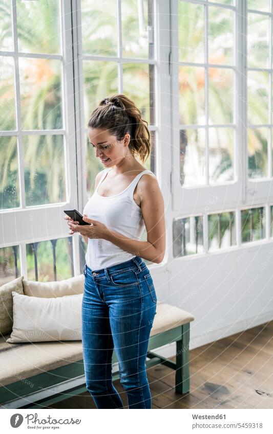 Smiling woman checking cell phone at the window at home mobile phone mobiles mobile phones Cellphone cell phones smiling smile windows females women telephones