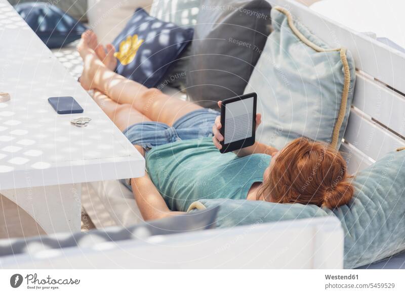 Young woman reading e-book, lying on bench E-book reader E-reader E-book device laying down lie lying down lounge lounges Lounge Room benches females women