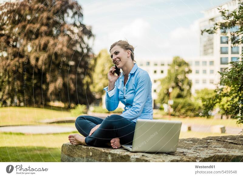 Smiling woman sitting in urban park talking on cell phone mobile phone mobiles mobile phones Cellphone cell phones on the phone call telephoning