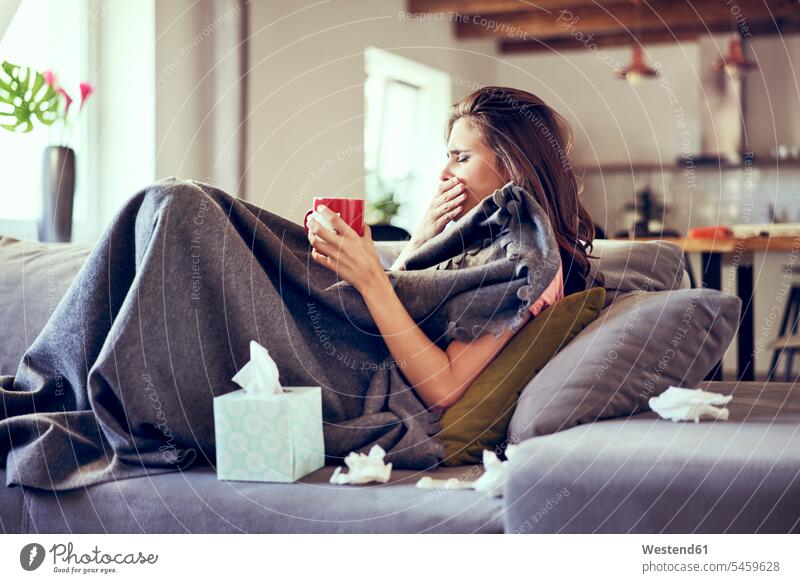 Portrait of woman lying sick on sofa coughing and trying to drink hot tea Tea Teas sitting Seated drinking young women young woman ill cold and flu influenza