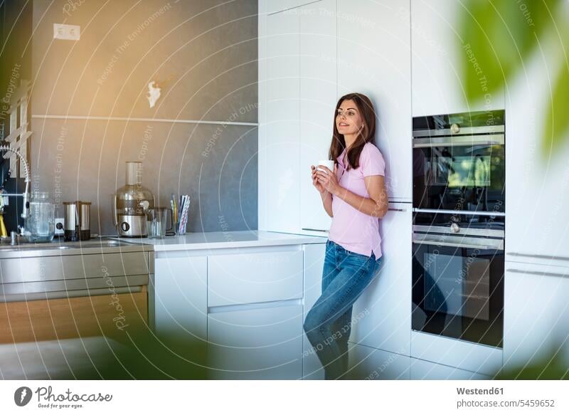 Smiling woman at home in kitchen with cup of coffee Coffee Coffee Cup Coffee Cups females women smiling smile Drink beverages Drinks Beverage food and drink