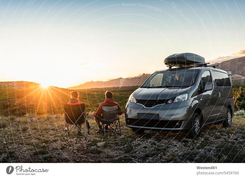 Man and woman sitting near camper van, looking at landscape at sunset outdoors location shots outdoor shot outdoor shots sunsets sundown atmosphere Idyllic