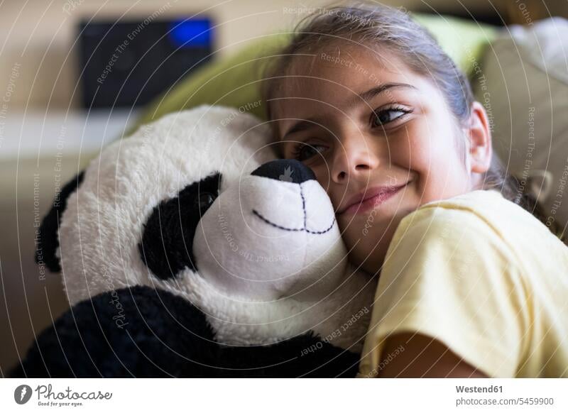 Little girl lying on couch at home cuddling with teddy panda bear snuggle cuddle snuggling koala koalas koala bears cuddly toy cuddly toys soft toy soft toys