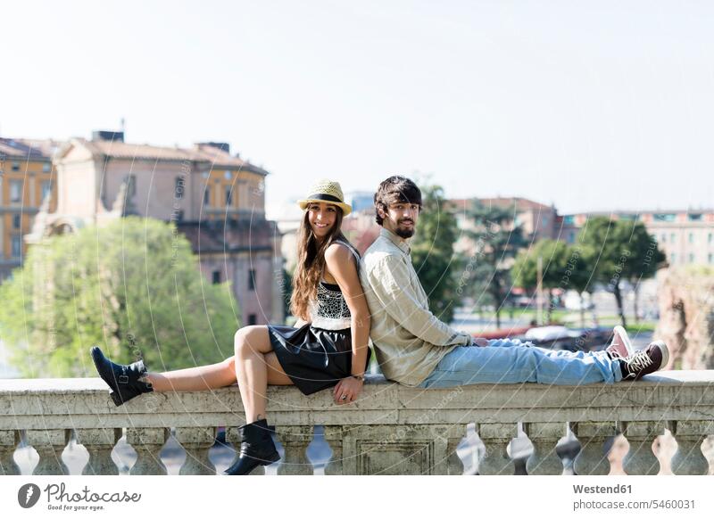 Happy young couple sitting back to back on balustrade Seated twosomes partnership couples parapet happiness happy people persons human being humans human beings