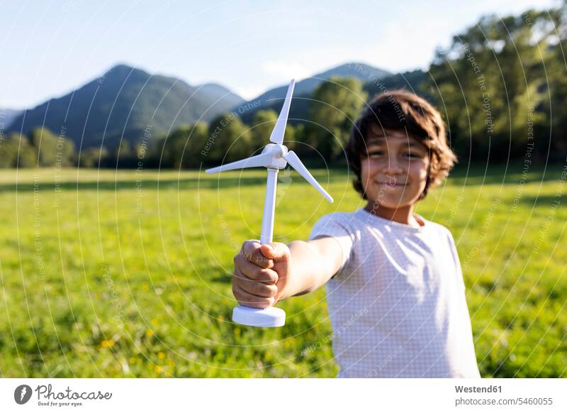 Smiling boy holding wind turbine toy while standing in meadow color image colour image outdoors location shots outdoor shot outdoor shots day daylight shot