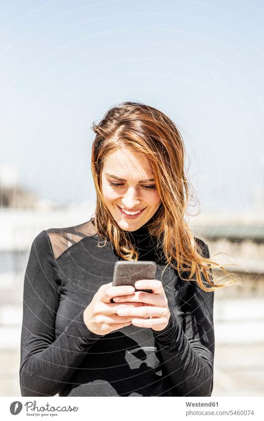 Portrait of smiling woman using smartphone outdoors females women use Smartphone iPhone Smartphones portrait portraits smile Adults grown-ups grownups adult