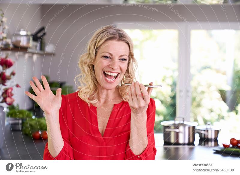 Exuberant woman using smartphone in kitchen domestic kitchen kitchens Smartphone iPhone Smartphones exuberance hilarity Frolic exuberant females women