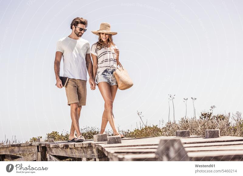 Young couple walking along a boardwalk from the beach touristic tourists bags go going smile seasons summer time summertime summery relax relaxing relaxation