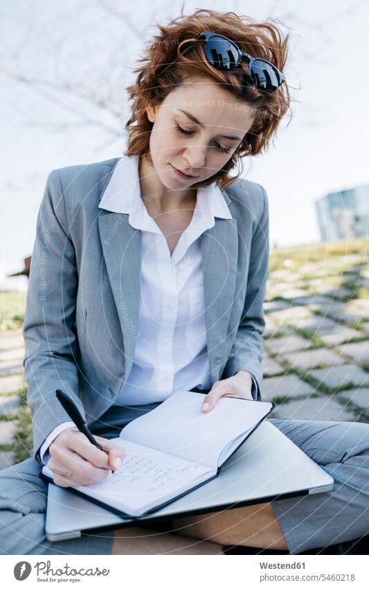 Businesswoman in the city, sitting on ground, writing in notebook Seated urban urbanity cross-legged tailor seat on the move on the way on the go on the road