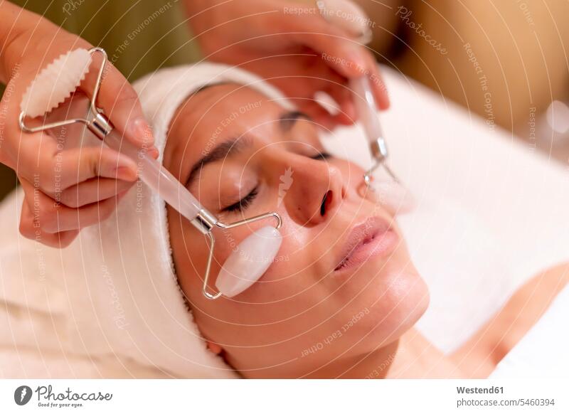 Young female customer receiving facial massage during treatment from beautician at spa color image colour image Spain indoors indoor shot indoor shots interior