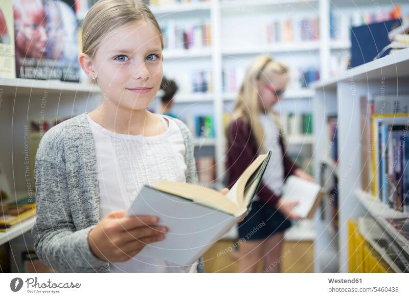 Portrait of smiling schoolgirl with book in school library books female pupils School Girl schoolgirls School Girls smile schools schoolchildren education