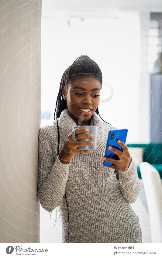 Smiling woman leaning on wall using smart phone while standing at home color image colour image indoors indoor shot indoor shots interior interior view