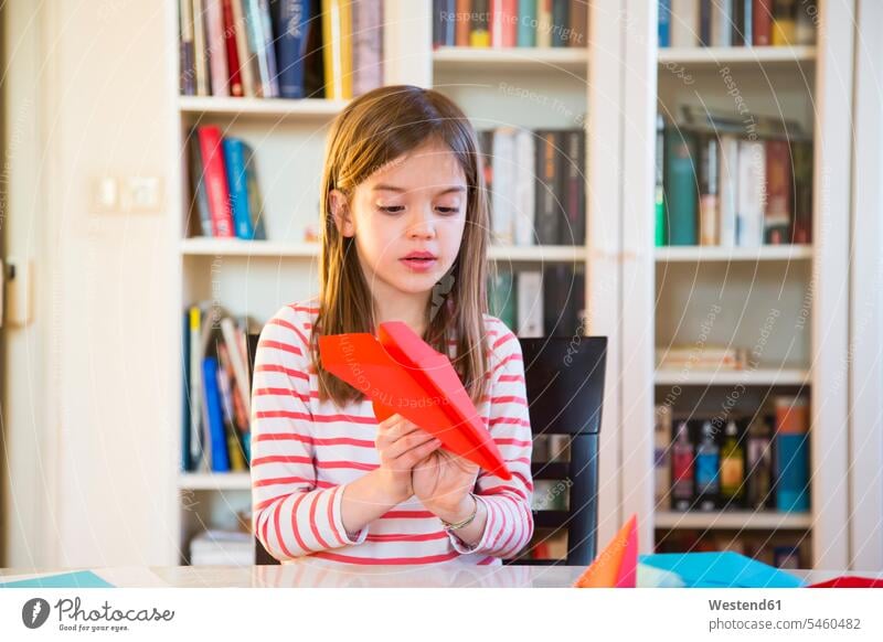 Girl tinkering paper plane on table at home Table Tables girl females girls crafting doing handicrafts paper dart paper planes paper darts paper aeroplane