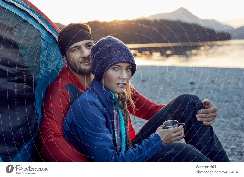 Young couple sitting at tent at lakeshore twosomes partnership couples Seated tents Lakeshore Lake Shore lakeside people persons human being humans human beings