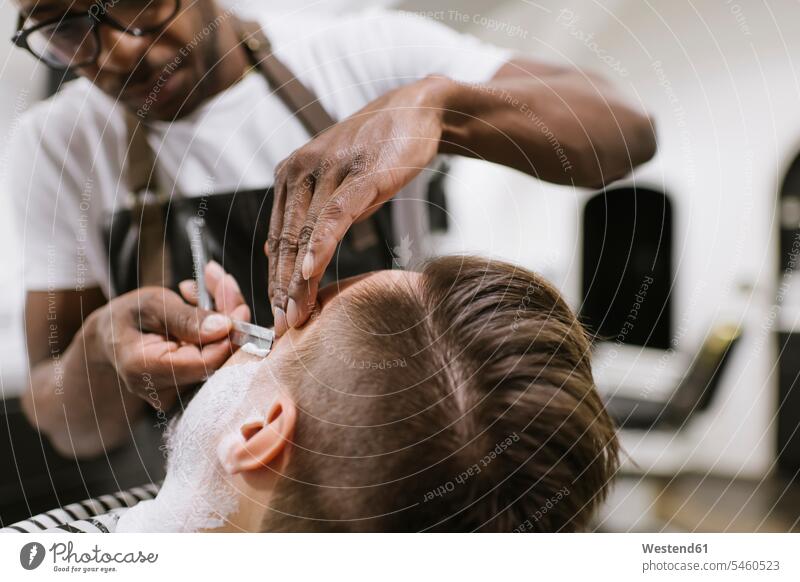 Man getting his beard shaved with razor in barber shop human human being human beings humans person persons African black black ethnicity coloured