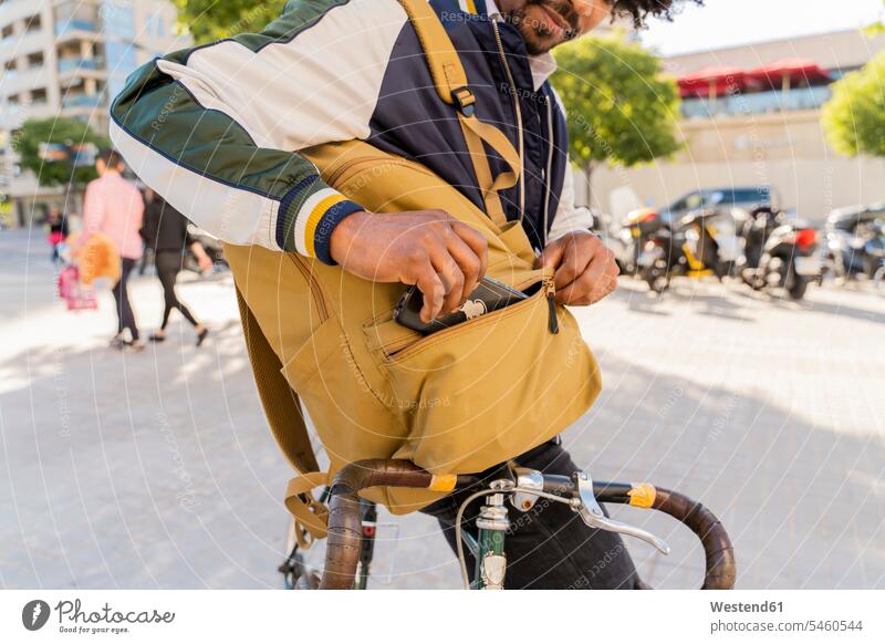 Casual businessman with bicycle taking cell phone out of backpack in the city, Barcelona, Spain business life business world business person businesspeople