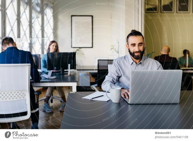 Hipster businessman working on laptop at desk in office Businessman Businessmen Business man Business men businesswear business attire business clothing