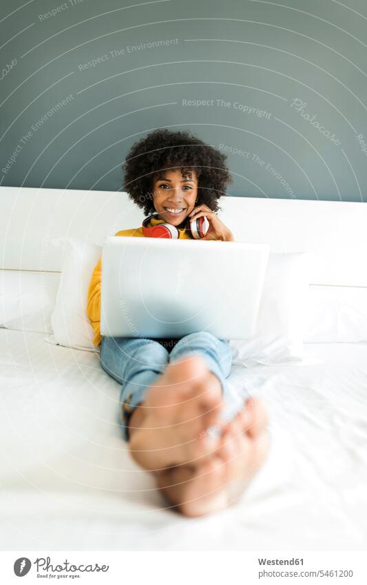 Happy woman lying on bed with headphones and laptop headset laying down lie lying down beds females women Laptop Computers laptops notebook happiness happy