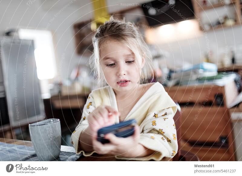 Portrait of little girl sitting at breakfast table in the kitchen using smartphone use Seated domestic kitchen kitchens females girls Breakfast Table