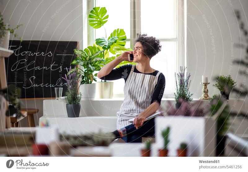 Smiling young woman on the phone in a small shop with plants Occupation Work job jobs profession professional occupation human human being human beings humans