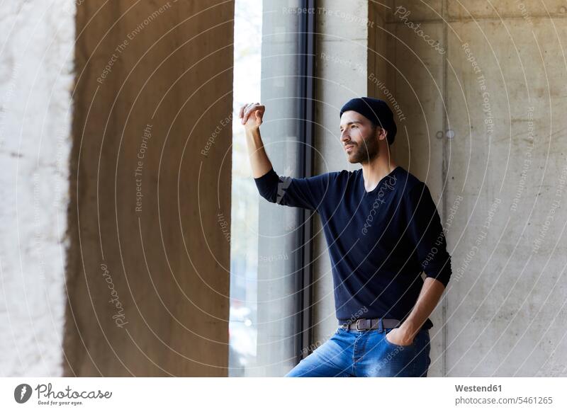 Young man wearing beanie looking out of window Germany concrete wall concrete walls thinking daydreaming dreamy lifestyle life styles Contemplation reflection