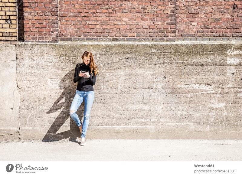 Woman with leaning against wall using cell phone Smartphone iPhone Smartphones woman females women use walls mobile phone mobiles mobile phones Cellphone