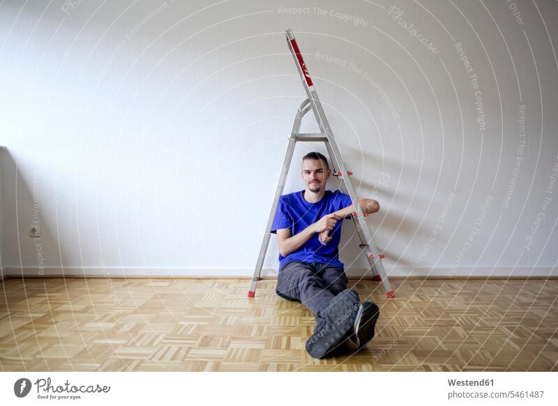 Young man sitting in an empty apartment T- Shirt t-shirts tee-shirt ladders smile Seated move moving Moving Home Contented Emotion pleased at home emptiness