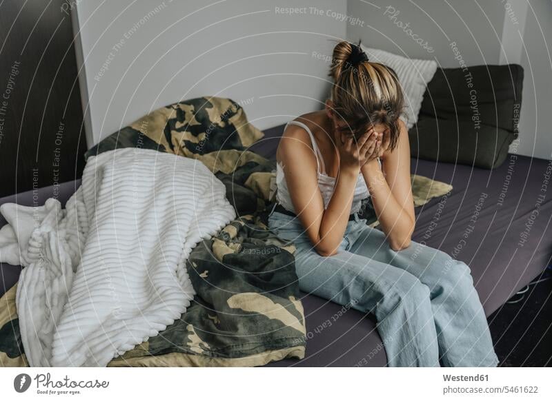 Despaired teenage girl sitting on bed, covering face with hands human human being human beings humans person persons Mixed Race mixed race ethnicity