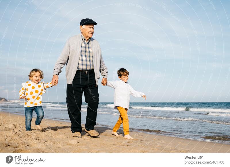 Grandfather strolling with his grandchildren hand in hand on the beach great-grandfather great-grandfathers brother brothers grandson grandsons granddaughter