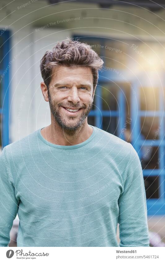 Portrait of smiling man in front of house with blue window men males windows houses smile portrait portraits Adults grown-ups grownups adult people persons