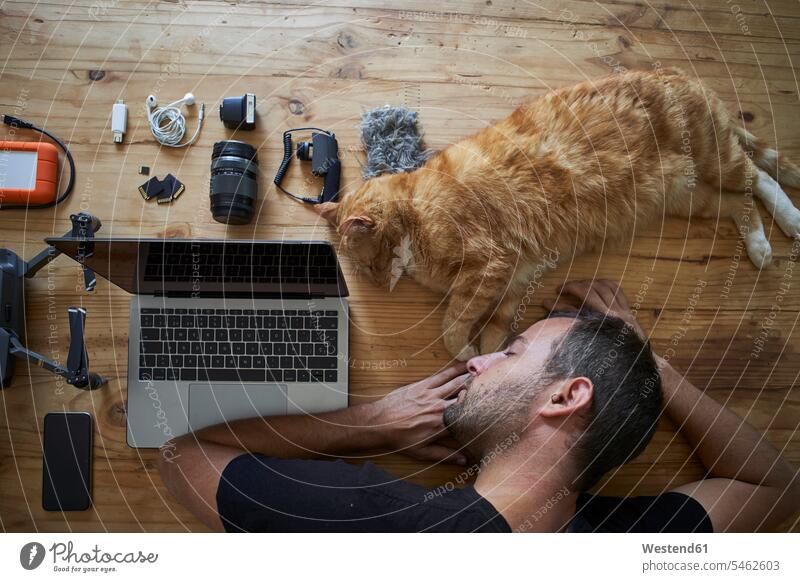 Exhausted man sleeping on table with ginger cat, laptop and photografic equipment Occupation Work job jobs profession professional occupation photographers