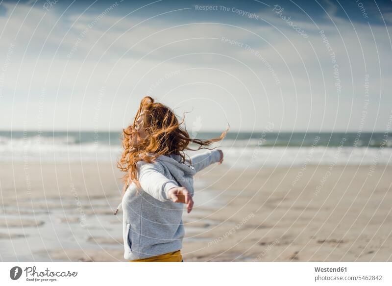 Redheaded woman relaxing on the beach, with arms outstretched females women carefree redheaded red hair red hairs red-haired beaches Adults grown-ups grownups