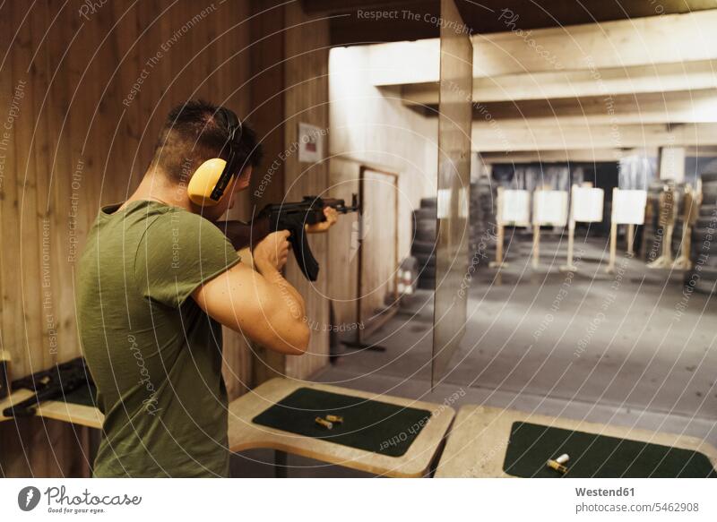 Man aiming with a rifle in an indoor shooting range gun guns rifles man men males weapon arms weapons shooting sports Adults grown-ups grownups adult people