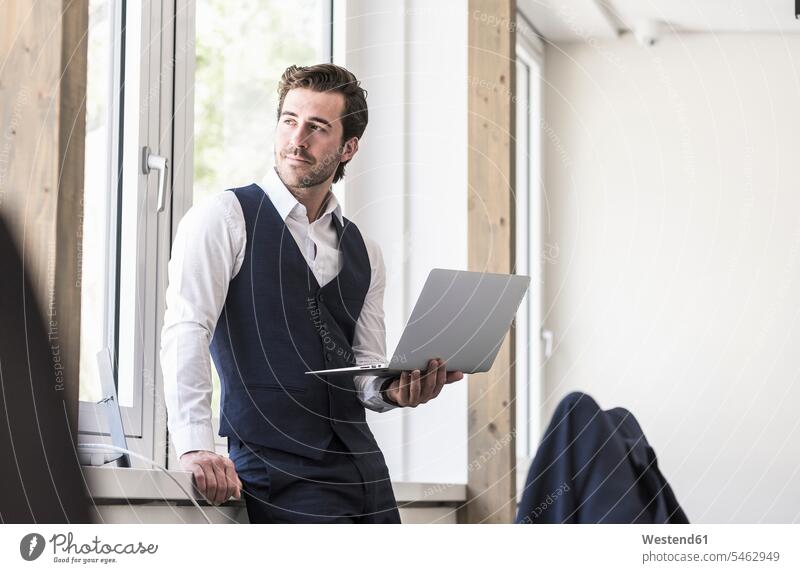 Businessman standing at the window, using laptop Occupation Work job jobs profession professional occupation business life business world business person