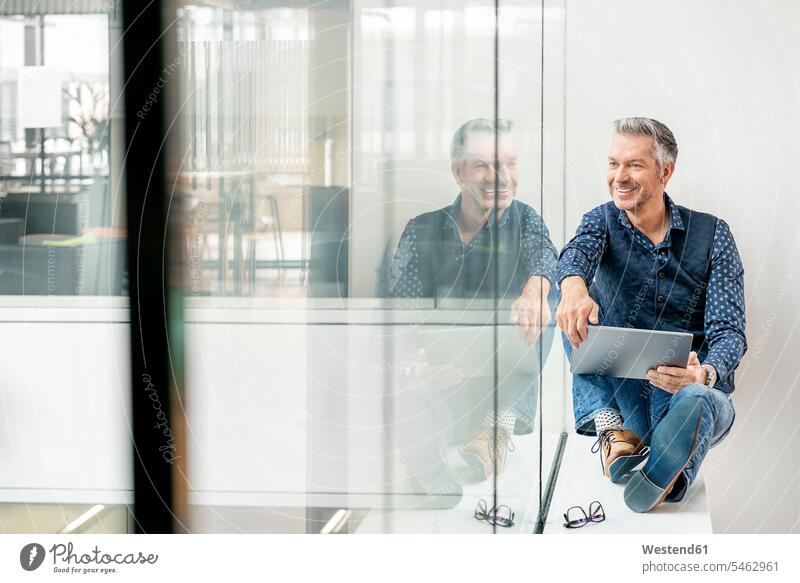 casual businessman sitting on windowsill in office building, using laptp human human being human beings humans person persons caucasian appearance