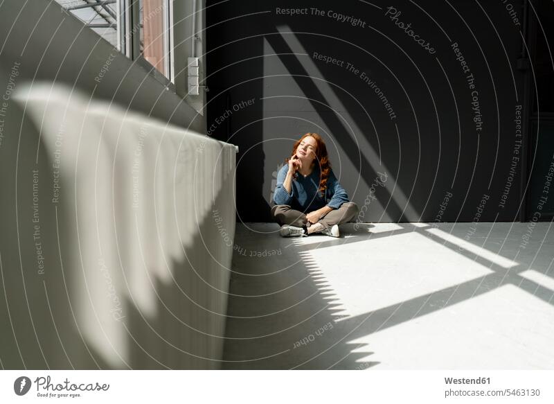 Redheaded woman sitting on floor of a loft enjoying sunlight human human being human beings humans person persons caucasian appearance caucasian ethnicity