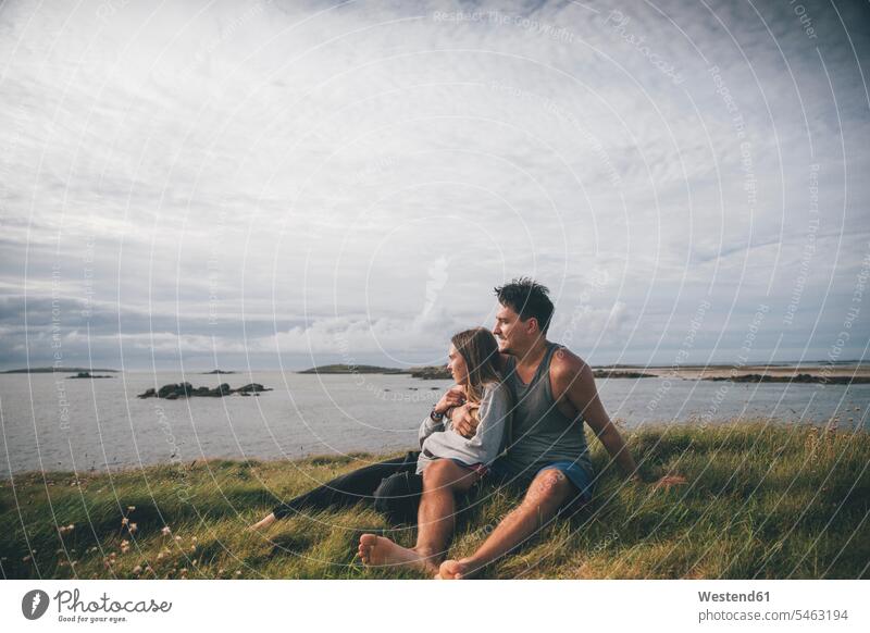 France, Brittany, Landeda, Dunes de Sainte-Marguerite, affectionate young couple sitting at the coast Affection Affectionate Seated twosomes partnership couples