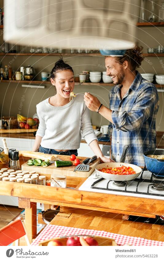 Young couple preparing food together, tasting spaghetti kitchen Food Preparation twosomes partnership couples taste cooking preparation prepare people persons