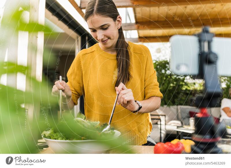 Smiling young woman filming with smart phone while preparing food at home color image colour image Germany casual clothing casual wear leisure wear