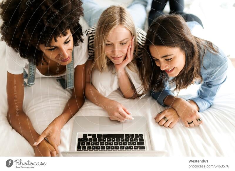 Three girlfriends lying on bed sharing laptop laying down lie lying down female friends beds Laptop Computers laptops notebook woman females women share mate