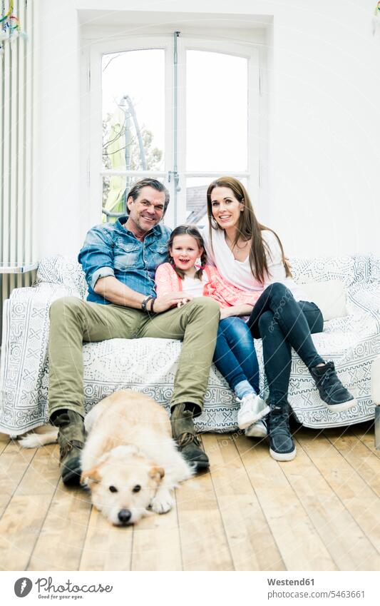 Portrait of happy family with dog in living room couch settee sofa sofas couches settees sitting Seated families portrait portraits dogs Canine happiness people