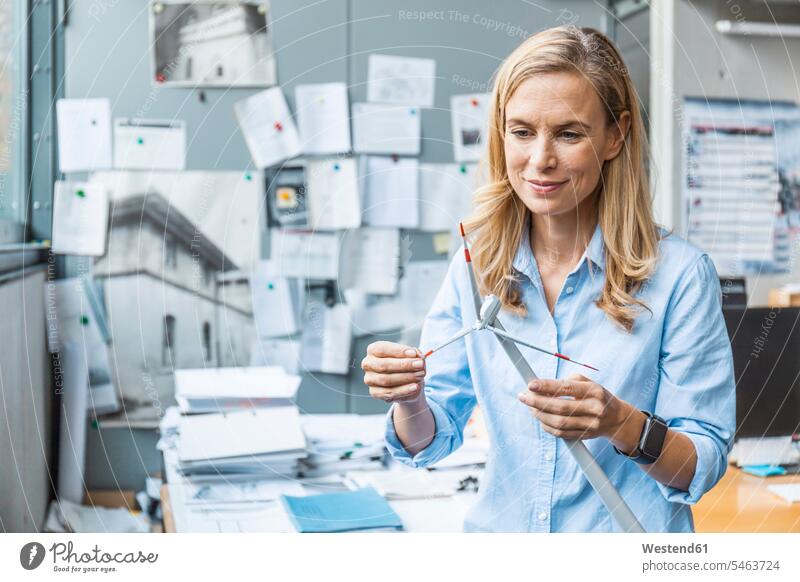 Confident woman in office holding wind turbine model confidence confident offices office room office rooms wind wheel windmills wind turbines wind wheels