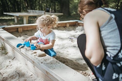 Mother playing with little daughter in sandbox on a playground sandpits sand-box sandboxes sand-boxes play yard play ground playgrounds mother mommy mothers ma