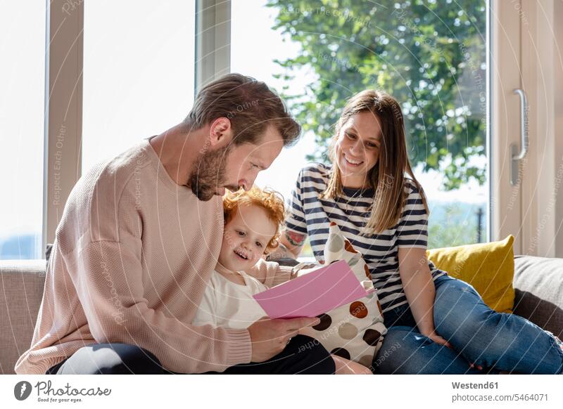 Smiling woman sitting and looking at man reading picture book to boy in living room color image colour image indoors indoor shot indoor shots interior