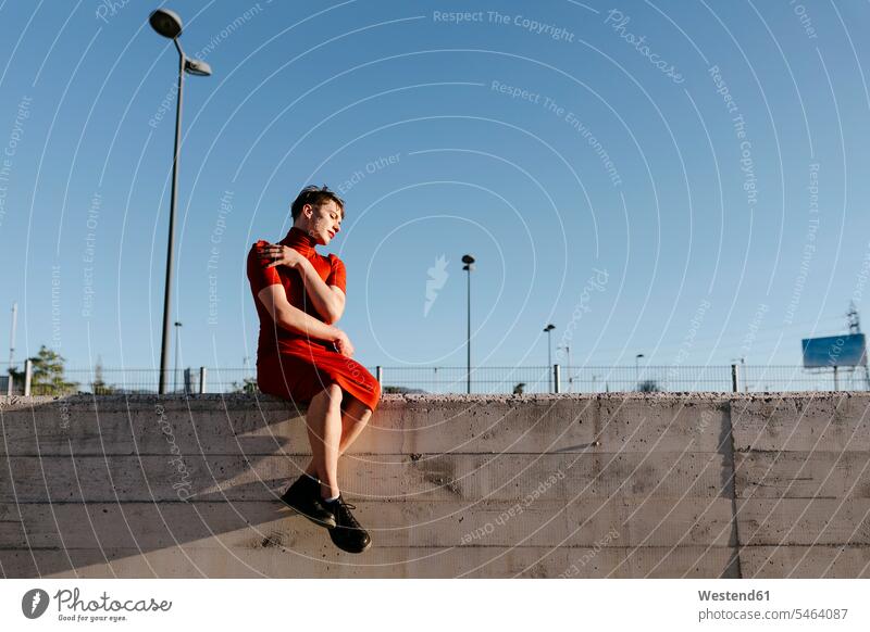 Non-binary man sitting on surrounding wall against clear sky color image colour image outdoors location shots outdoor shot outdoor shots day daylight shot